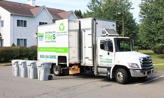 A FileShred mobile shredding truck parked in a lot next to some secure shredding bins