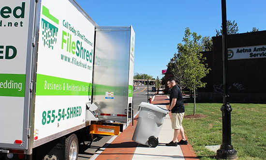 A mobile shredding employee wheeling a shredding bin to the mobile shredding truck