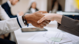 A business handshake over a desk with papers on it.