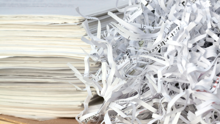 Shredded paper beside stacks of documents ready for secure destruction.